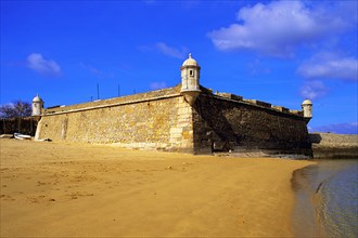 Golden sand on the beach at Lagos, with the old harbour defenses, the 17th century Forte Bandeira,