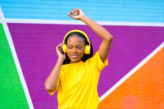 African woman dancing while listening to music against a colorful wall in the city