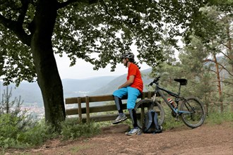 Mountain biker taking a break on a bench in the Palatinate Forest near the Weinbiet above Neustadt