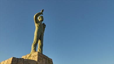Statue of a man pointing to the sky, standing on a pedestal, bronze statue of a waving sailor in