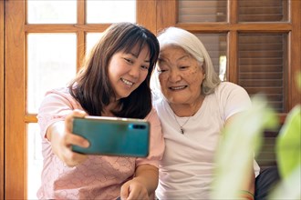Loving daughter taking selfie using mobile phone with mother at home. Japanese family