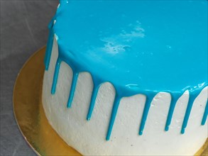 A white frosted cake with vibrant blue icing dripping down the sides on a gold base