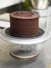A simple chocolate cake on a cake stand, coated with rich chocolate icing