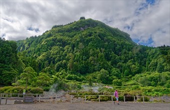 Tourists visit an area of volcanic activity surrounded by green mountains and plumes of steam,