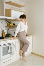 Young barefoot woman standing by the countertop of a well-lit and elegantly designed modern kitchen