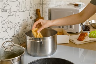 Female hand adds pappardelle pasta into pot with boiling water