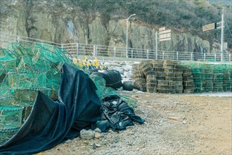 Lobster traps stacked in gravel lot with mountain cliff in background in South Korea