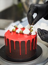 Finishing touches being applied to a chocolate cake with red dripping icing and golden balls