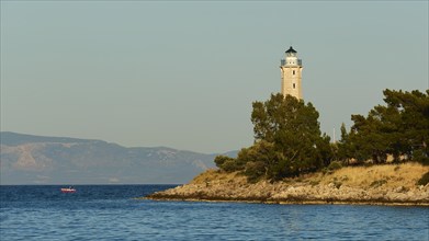 Lighthouse on a cliff surrounded by pine trees with calm sea in the evening light, Gythio, Mani,