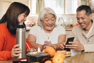 Adult children teach their elderly mother of Japanese origin how to use a cell phone while sitting