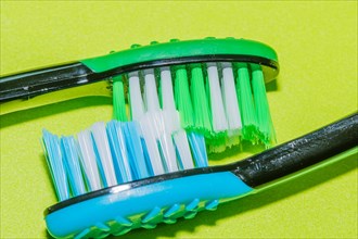 Bristles of one blue and one green toothbrushes interlocked on green background
