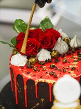 Close-up of a decadent cake being decorated with roses, meringues, and gold accents