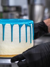 A pastry chef applying blue icing on a white cake, highlighting the baking process in a kitchen