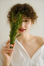 Cute young woman covers her eye with rosemary branch