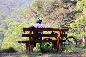 Mountain biker taking a break on a bench in the Palatinate Forest near the Weinbiet above Neustadt