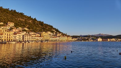 The setting sun bathes the coastal town in a warm light with reflections in the water, Taygetos