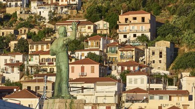 Statue raises its arm over a Mediterranean settlement with densely packed houses, Gythio, Mani,