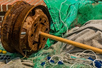 Rusted metal automobile wheel with attached yellow pole laying among fishing nets and debris in