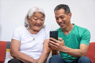 Adult son teaching his elderly mother of Japanese origin how to use a mobile phone. Elderly mother