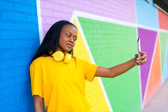 Side view portrait of a young african woman posing taking a selfie leaning on a colorful wall