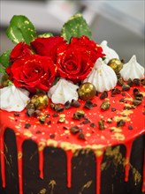 Side details of a decorated cake with roses, dripping red glaze, and chocolate sweets