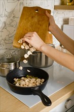 Woman adding chopped champignon to a frying pan in the kitchen