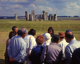 Group of Japanese tourists with guide visiting Stonehenge monument at Salisbury, England, UK,