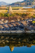 Rock cairn on edge of canal reflected in calm blue water in South Korea