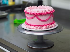 A round cake with pink ruffled frosting on a rotating cake stand