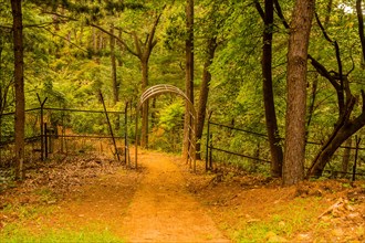 Path to chrome gate in wire fence at edge of wooded public park in South Korea