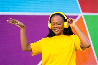 Smiling african young woman dancing while listening to music outdoors next to a multicolored wall
