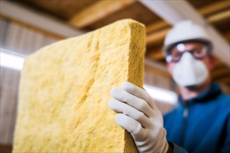 Construction worker installing mineral wool filling used as isolation material in walls. KI