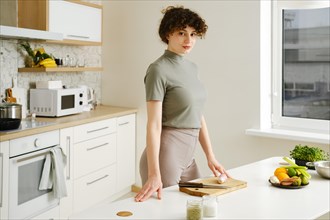 Woman stands in a well-lit modern kitchen preparing ingredients on a table. Young woman is ready to