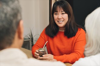 Portrait of Asian woman in red sweater drinking mate and conversing with two unrecognizable people