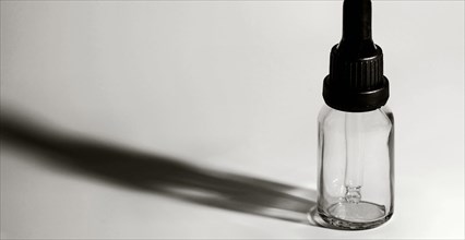 Closeup of single eye dropper bottle with strong dark shadow on white background