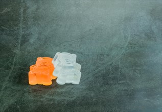 One orange, one white homemade bar of soap made to resemble toy bear on black textured background