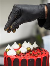 A professional pastry chef wear black gloves artfully decorating a chocolate cake with golden