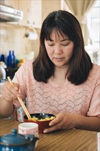 Closeup of asian young woman eat rice with chopsticks at home