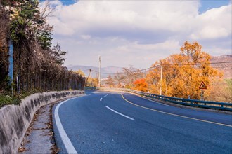 Three lane mountain road with slower traffic lane under a cloudy sky on autumn day in South Korea