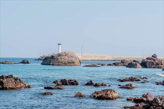 Large boulders in ocean in front of white lighthouse on concrete pier