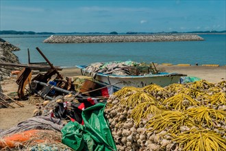 Small fishing boat filled with nets and gear beached among assortment of fishing paraphernalia in