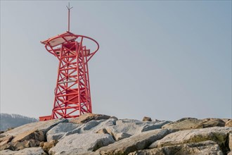 Red steel warning beacon on pier of large boulders at rural fishing port in South Korea