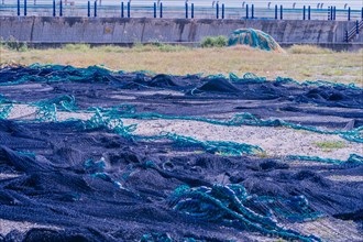 Large black fishing net laid out to dry in gravel lot in front of sea wall in South Korea