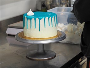A partially decorated cake with blue icing on a rotating cake stand in a kitchen