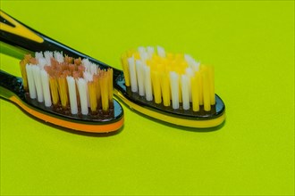 Closeup of two toothbrushes in orange and yellow on a green background
