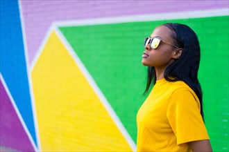 Side view of a serious cool african woman with sunglasses next to a colorful wall