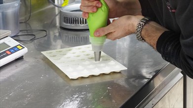 Chef piping cream onto a baking silicon mold sheet in a professional kitchen setting