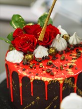An opulent cake with red glaze, rose toppings, and gold brush details