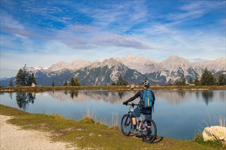 Mountain biker taking a break at the Kaltwassersee lake in Seefeld/Tyrol. The snow-covered peak on