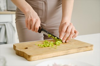 Unrecognizable woman chopping fresh celery on wooden board while preparing food